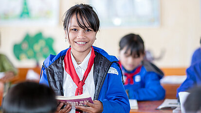Bild: Mädchen aus Vietnam ist in ihrem Klassenzimmer und hält ein Buch in den Händen.