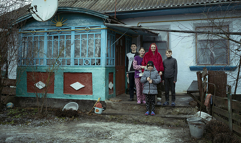 Eine Frau steht mit ihren vier Kindern vor einem Haus.