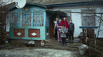 Eine Frau steht mit ihren vier Kindern vor einem Haus.