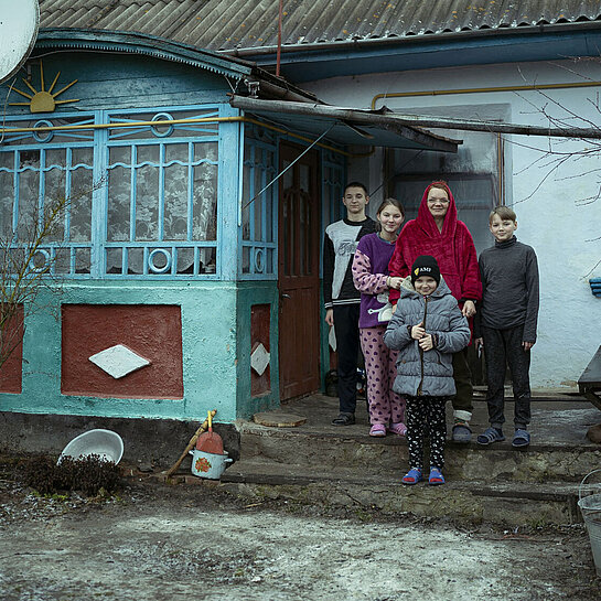 Eine Frau steht mit ihren vier Kindern vor einem Haus.