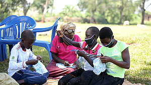 Kinder und eine Frau in Uganda nähen gemeinsam waschbare Hygieneartikel im Freien