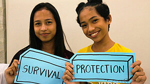 Zwei Mädchen halten Schilder mit der Aufschrift ‚Survival‘ und ‚Protection‘ – Engagement für Kinderrechte im Projekt gegen Kinderhandel auf den Philippinen.