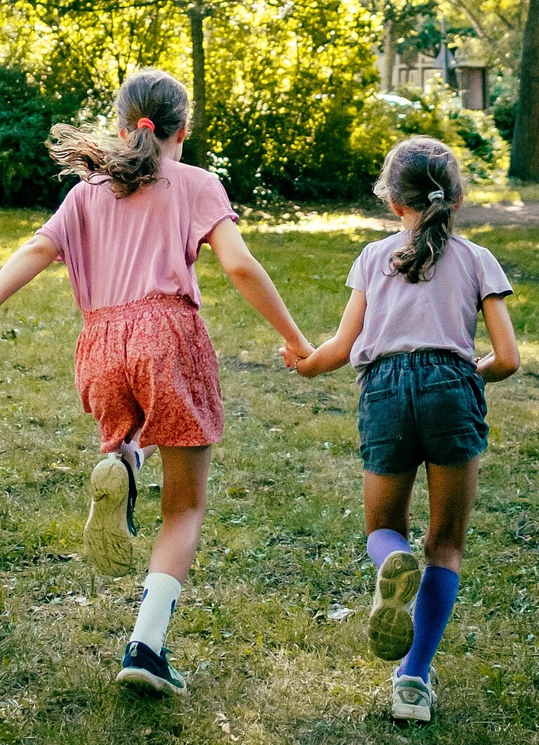 Zwei Mädchen rennen Hand in Hand über eine Wiese