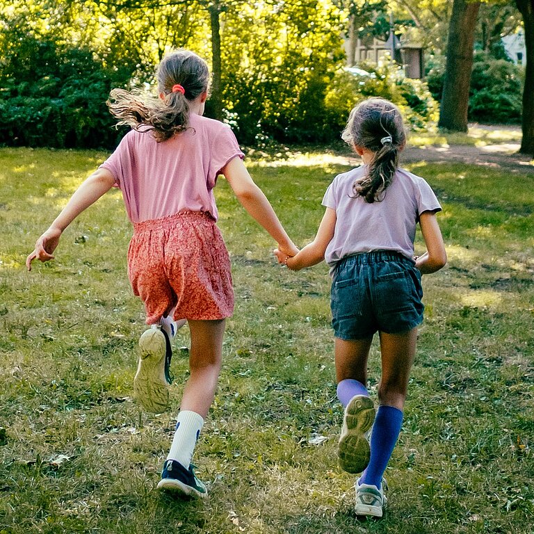 Zwei Mädchen rennen Hand in Hand über eine Wiese