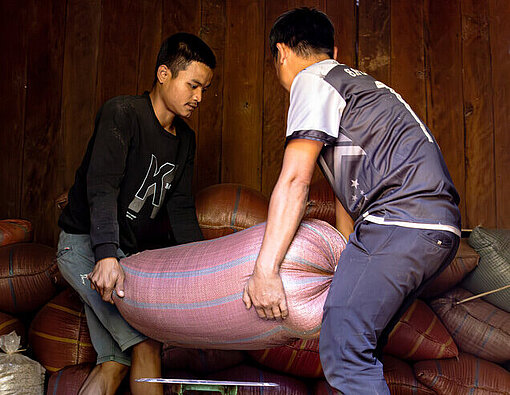 Zwei Männer heben Reissack auf Waage