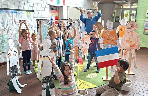 Kinder und ein Mann stehen zwischen lebensgroßen Fußballspielern gebastelt aus Papier.