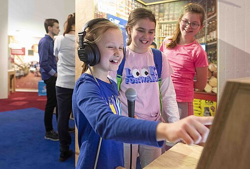 Im Stadtmuseum Ingolstadt können beim Besuch von „Mission 2030“ sieben Länder auf vier Kontinenten interaktiv erkundet werden Drei Besucherinnen amüsieren sich an einer interaktiven Ausstellungsstation, die sie ausprobieren