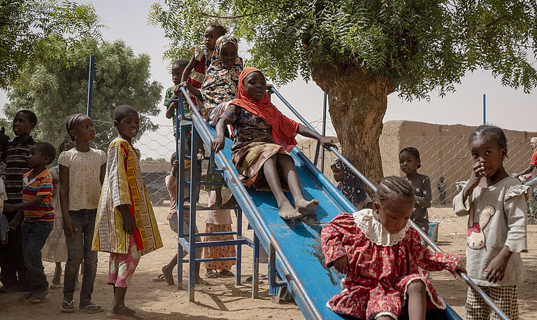 Eine Gruppe Kinder auf einem Spielplatz. Sie stehen an einer Rutsche Schlange und rutschen.
