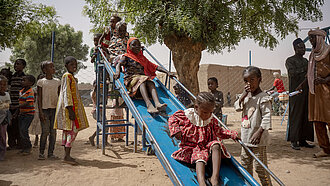 Eine Gruppe Kinder auf einem Spielplatz. Sie stehen an einer Rutsche Schlange und rutschen.