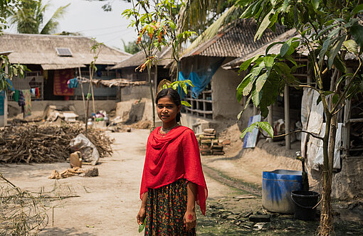 Ein jugendliches Mädchen aus Bangladesch steht vor einigen Hütten