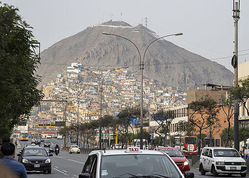 In der Acht-Millionen-Metropole Lima liegen einige Bezirke an den umliegenden Bergen Im gelben Nachmittagslicht ist eine Siedlung einfacher bunter Häuser an einem steilen Berghang zu sehen
