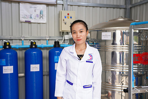 Eine Frau steht vor einem Wasserfiltrationssystem in einem Gesundheitszentrum, das sauberes Trinkwasser bereitstellt.