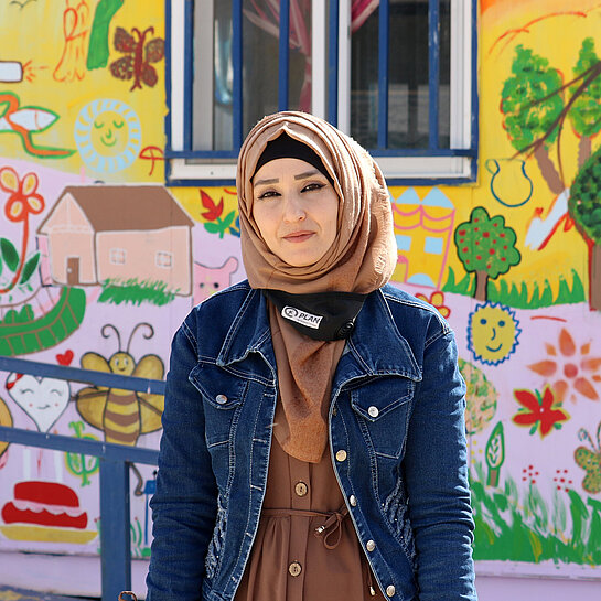 Alia, eine junge Frau, steht vor einem bunt bemalten Gebäude.