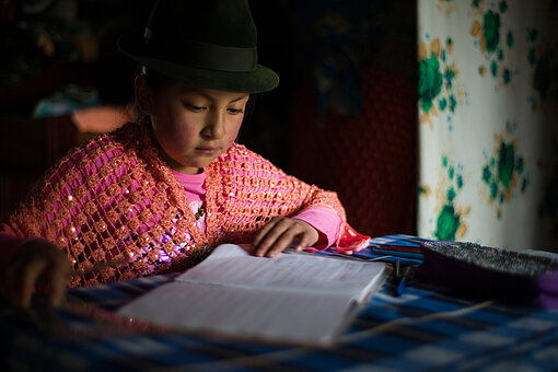 Ein Mädchen sitzt an einem Tisch un liest in einem Schulheft