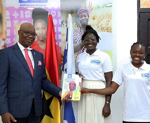 Zwei jugendliche Mädchen überreichen dem Landesdirektor von Plan International Ghana die ausgedruckte Jugenddeklaration