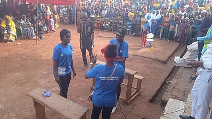 Drei junge Frauen mit Shirts von Plan International sprechen vor einer Gruppe