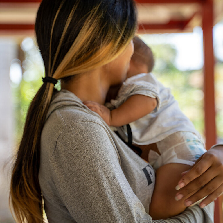 Eine Frau hält ein Baby im Arm, sie ist nur von der Seite zu sehen