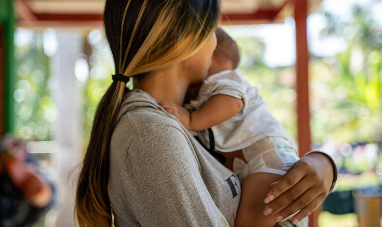 Eine Frau hält ein Baby im Arm, sie ist nur von der Seite zu sehen