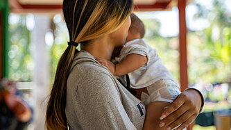 Eine Frau hält ein Baby im Arm, sie ist nur von der Seite zu sehen