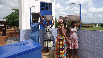 Frauen in Ghana füllen an einer öffentlichen Wasserstelle große Schüsseln mit sauberem Trinkwasser