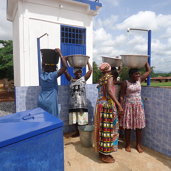 Frauen in Ghana füllen an einer öffentlichen Wasserstelle große Schüsseln mit sauberem Trinkwasser