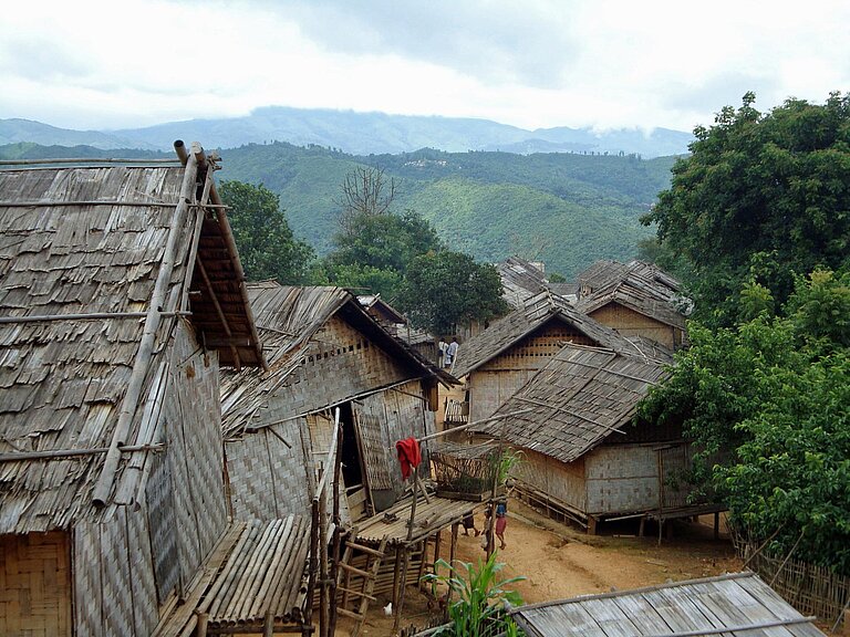 Strohgedeckte Hütten vor einem Waldgebiet