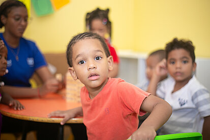 Ein Junge sitzt mit andern Kindern um einen Schultisch