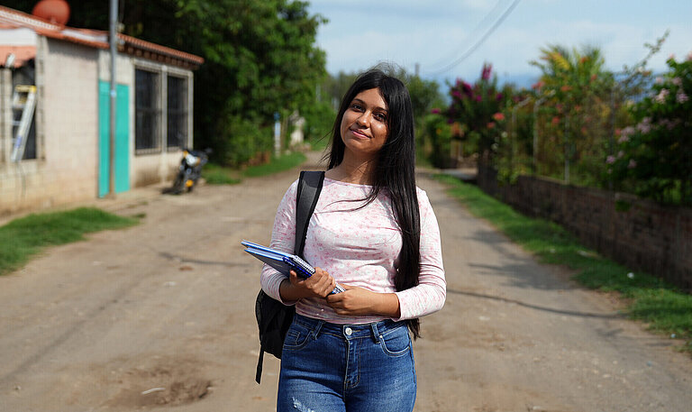 Teenagerin trägt Schulrucksack und Notizblock, unterwegs in einer ländlichen Gegend. Bildung als Schlüssel für die Zukunft.