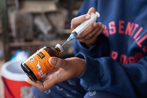 Nahaufnahme auf die Hände, in einer Hand ist eine kleine Flasche, mit der anderen Hand wird eine Spritze mit Flüssigkeit aus der Flasche aufgezogen