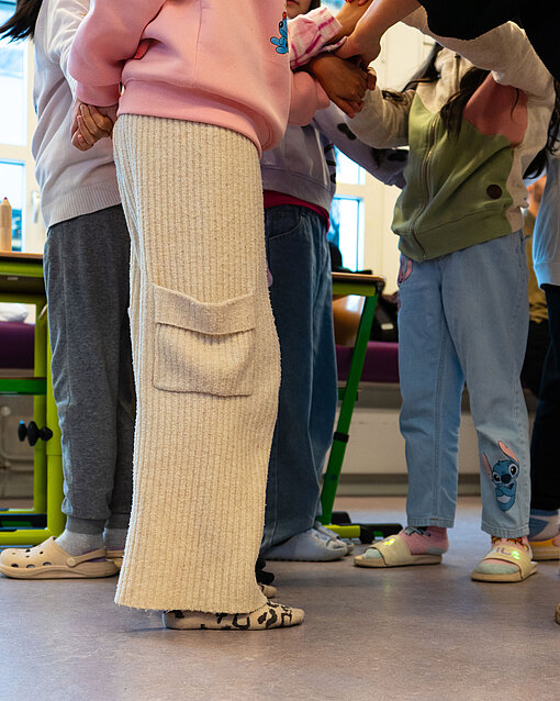 Kinder führen eine Übung im Rahmen des Projekts "Stark in die Zukunft" durch, bei der sie sich ver- und entknoten, um Teamfähigkeit und Zusammenhalt zu fördern.