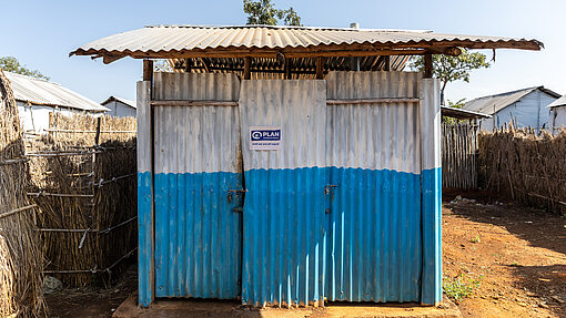 Die sanitären Anlagen/Toiletten haben ein Wellblechdach und Wellblechwände, die in Weiß und Blau gestrichen sind.