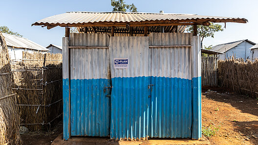 Die sanitären Anlagen/Toiletten haben ein Wellblechdach und Wellblechwände, die in Weiß und Blau gestrichen sind.