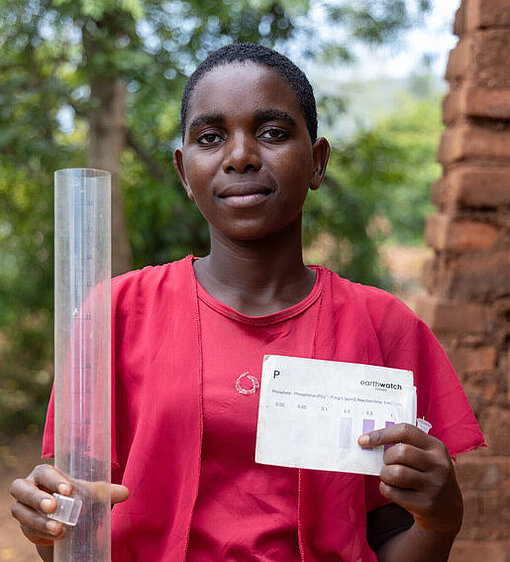 Liness steht mit den benötigten Utensilien für eine Wasserprobe in ihrer Gemeinde