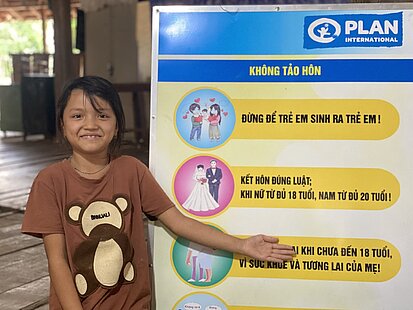 Ein Mädchen zeigt auf ein Plakat zum Thema Frühverheiratung