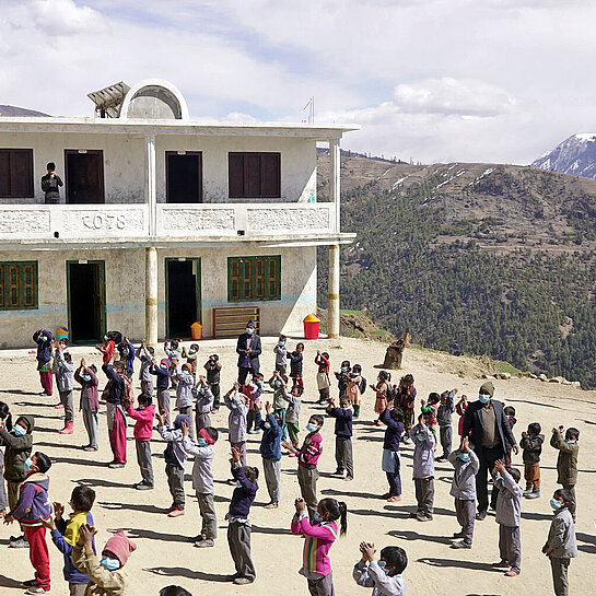 Auf einem Platz vor einem Schulgebäude im Himalaja-Gebirge stehen Schulkinder