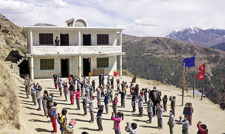 Auf einem Platz vor einem Schulgebäude im Himalaja-Gebirge stehen Schulkinder