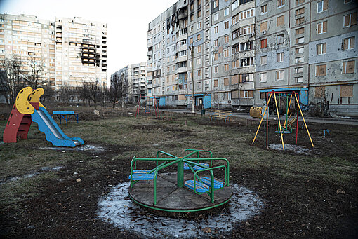 Ein leerer Spielplatz vor zerstörten Häusern