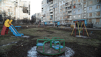 Ein leerer Spielplatz vor zerstörten Häusern