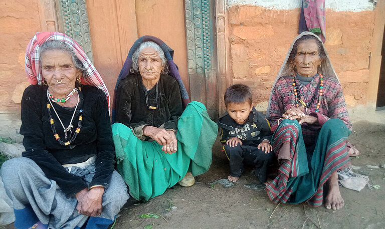 Drei alte Frauen sitzen vor einem Haus und ein kleiner Junge sitzt bei ihnen