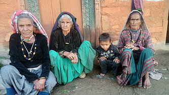 Drei alte Frauen sitzen vor einem Haus und ein kleiner Junge sitzt bei ihnen