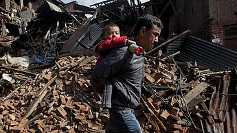 Ein Mann trägt sein Kind durch die Trümmer © AP Photo / Niranjan Shrestha