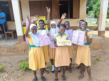 Mädchen halten Pakete mit Menstruationsartikeln und winken