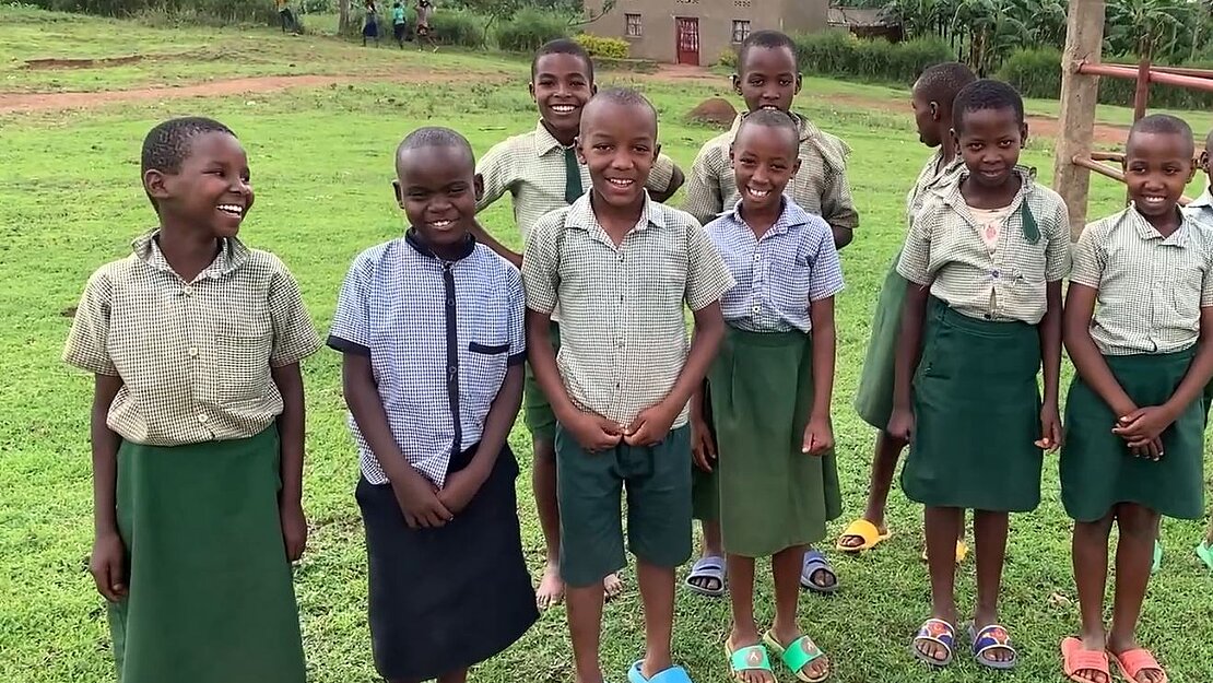 Eine Gruppe Kinder steht auf einer Wiese, sie lächeln in die Kamera