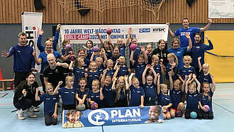 Eine große Gruppe Mädchen in Handball Trikots steht vor einem Tor zum Gruppenfoto zusammen. 