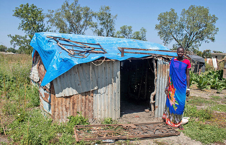 Eine junge Frau steht vor einer Wellblechhütte in Südsudan