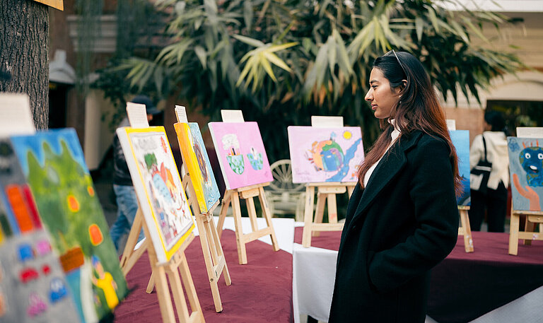 Eine Frau schaut sich eine Reihe von Bildern an, die auf Staffeleien ausgestellt sind.