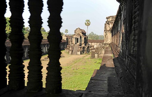 Blick aus dem Fenster auf die massiven Steinmauern einer Tempelanlage umgeben von grünen Wäldern