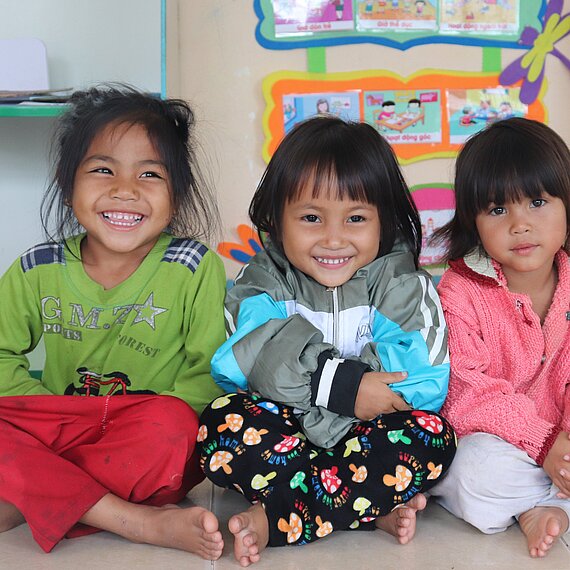 Drei Mädchen sitzen im Schneidersitz nebeneinander und lächeln