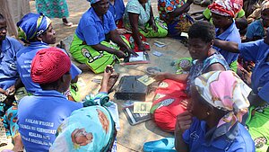 Frauen in Malawi bei einer Schulung zur finanziellen Bildung und gemeinschaftlichen Spargruppen, mit Bankbüchern und Karten in der Hand