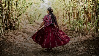 Ein Mädchen mit breitem, schwingendem Rock geht eine Allee entlang 